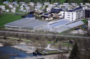 Luftaufnahme einer Produktionsgärtnerei mit mehreren Gewächshäusern, Wohnhäusern und einem angrenzenden Campingplatz am