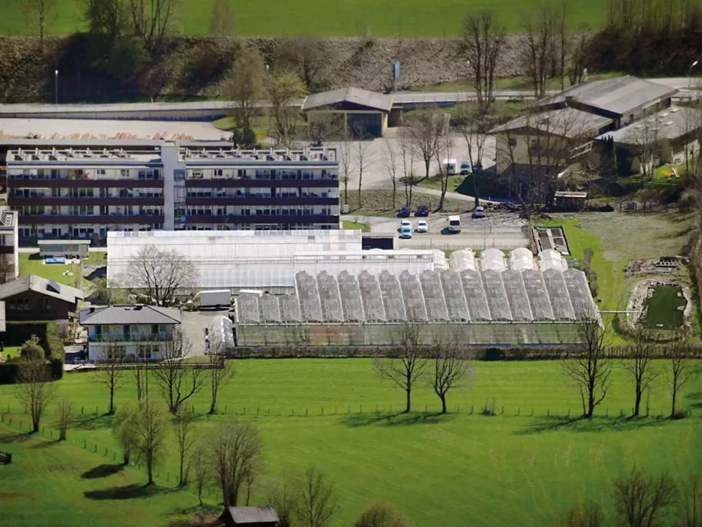 Luftaufnahme einer Produktionsgärtnerei mit Gewächshäusern, Bäumen und angrenzenden Gebäuden in Sankt Johann im Pongau